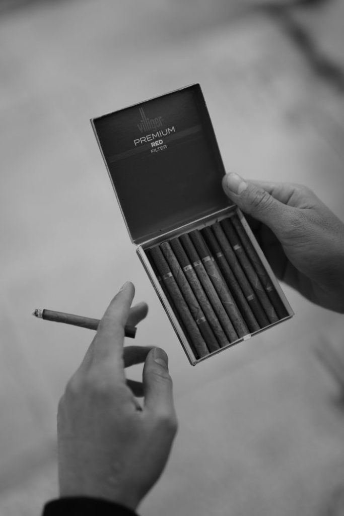 Hands holding a box of premium cigarettes with one cigarette taken out.