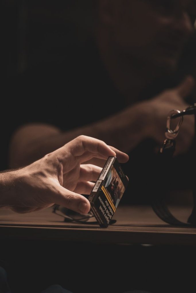 Close-up of a hand holding a cigarette pack, emphasizing the habit and addiction theme.