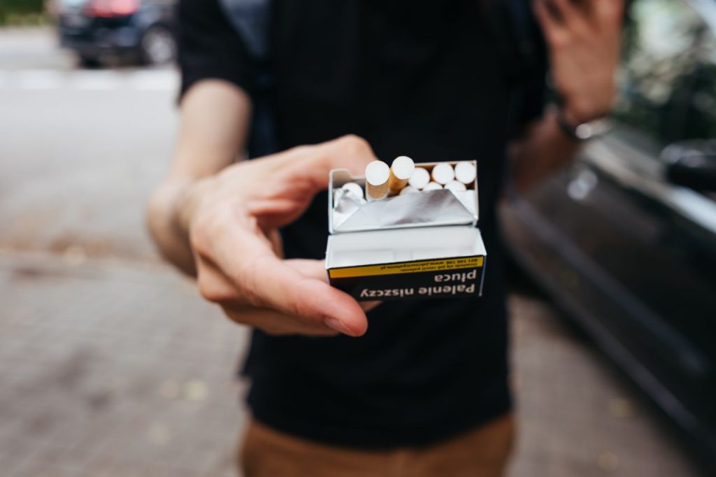 Close-up of a man offering a pack of cigarettes outdoors on a city street.