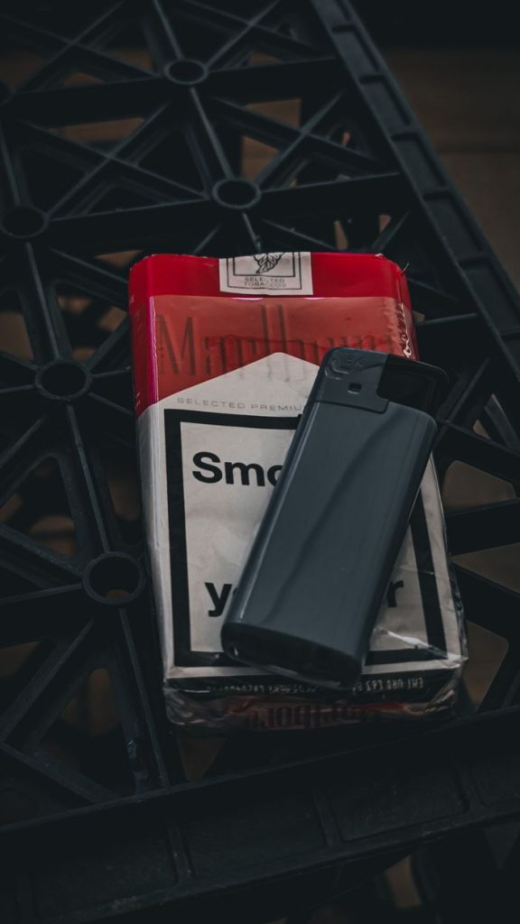 Close-up of a red and white cigarette pack with a black lighter on a textured surface.