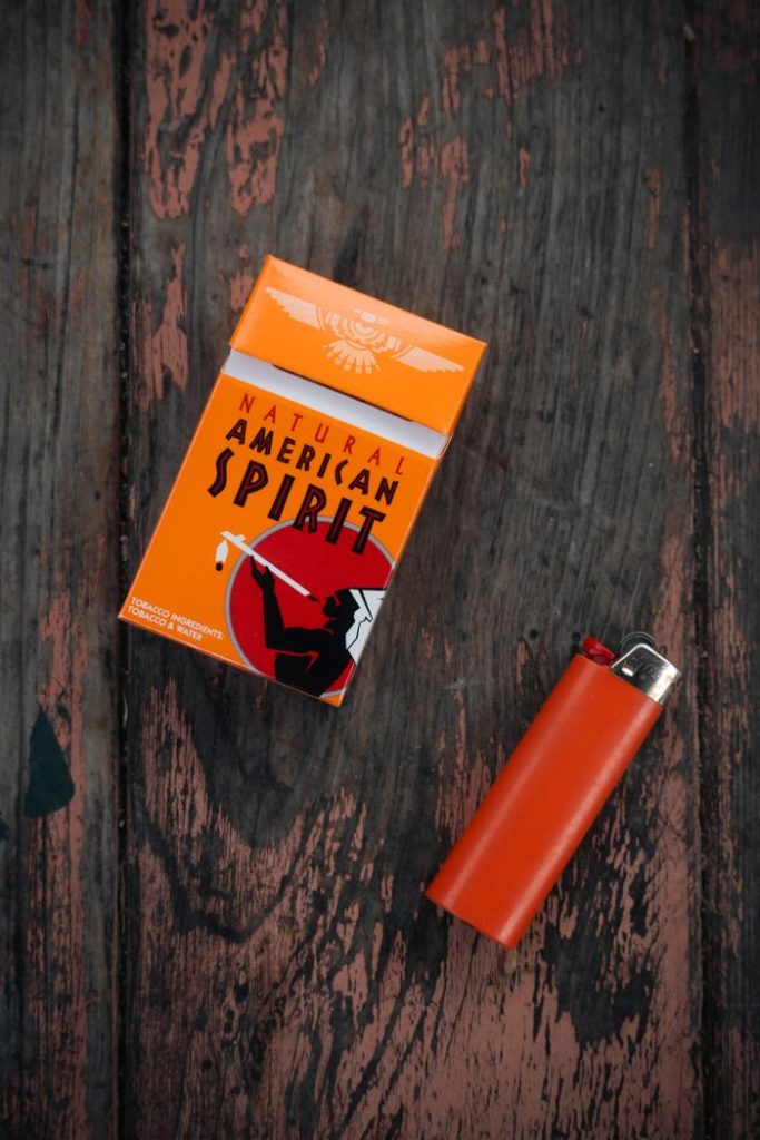 An artistic shot of a cigarette pack and a lighter placed on a rustic wooden surface.