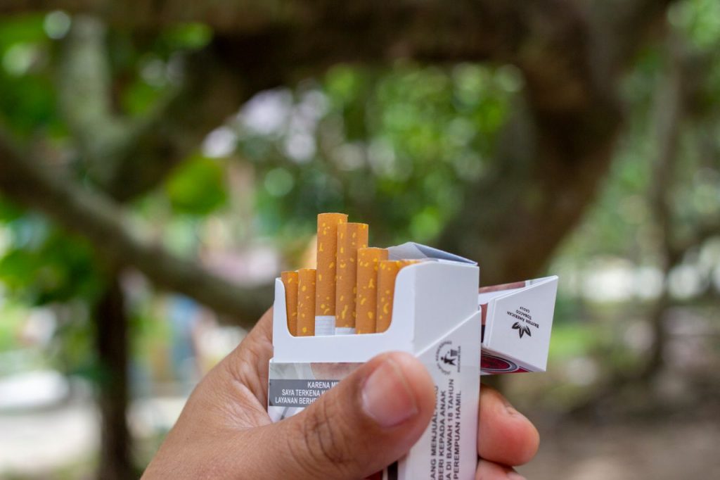 Close-up of a hand holding an open pack of cigarettes in a natural outdoor setting.