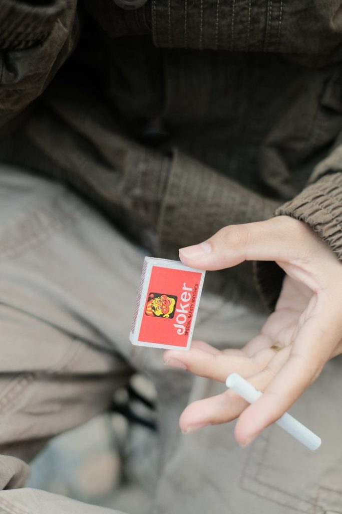 Close-up of a hand holding a joker matchbox and cigarette.