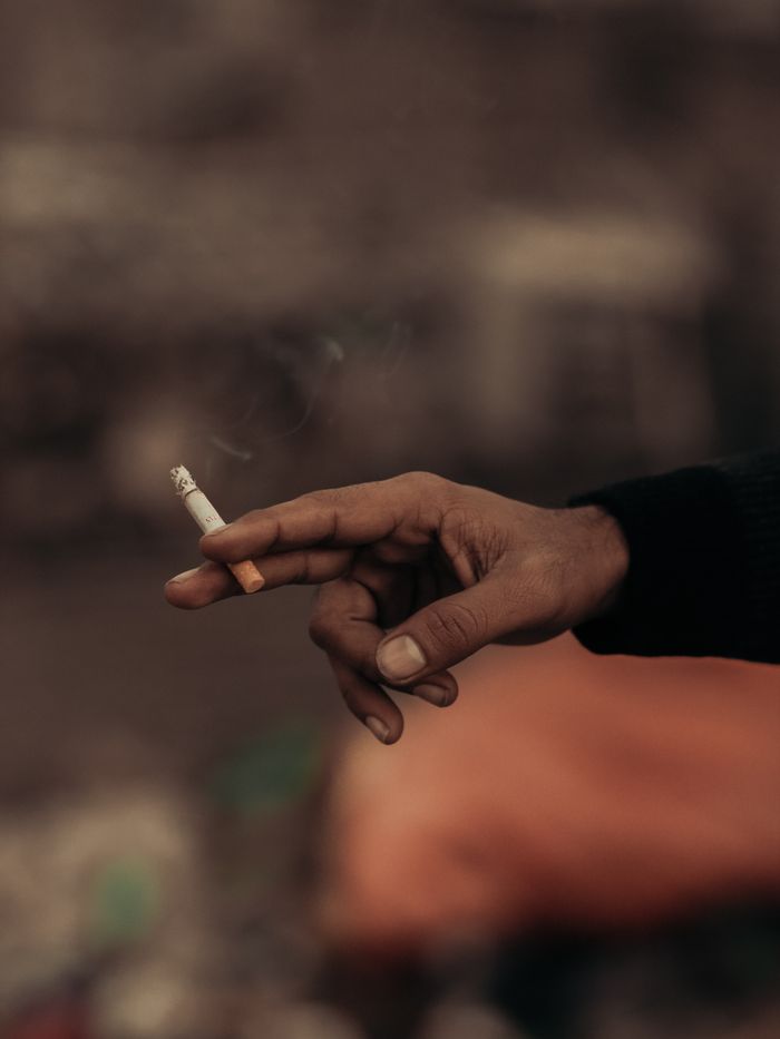 A close-up shot showcasing a hand holding a cigarette with a blurred outdoor background.