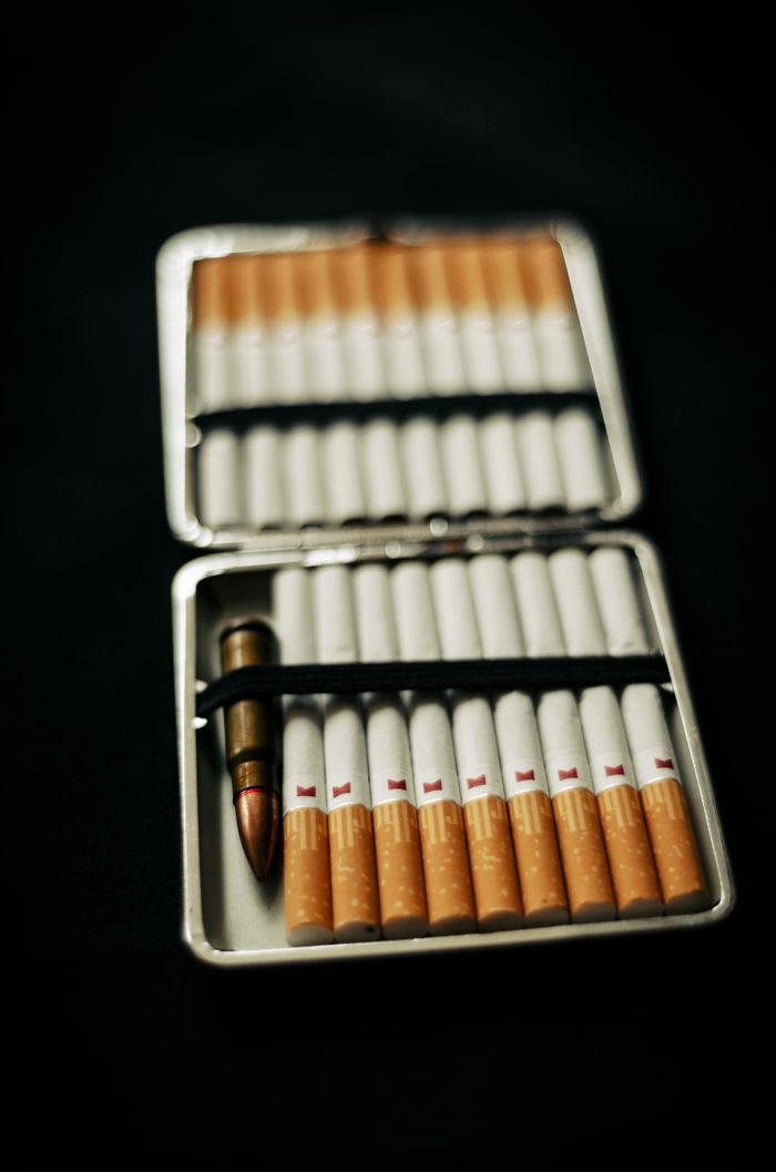 A cigarette case containing cigarettes and a bullet against a dark background.