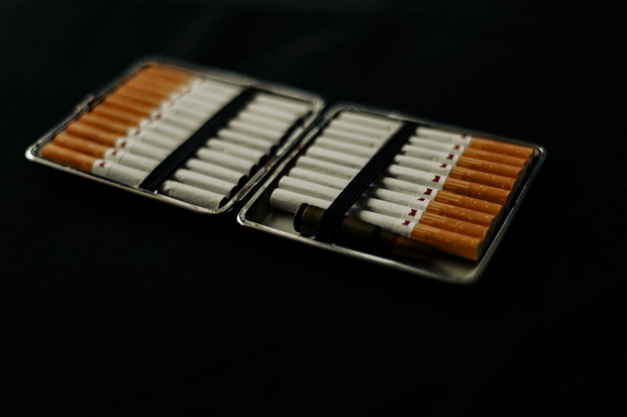 An open cigarette case filled with cigarettes, placed on a dark surface, conveying a mood of smoking and lifestyle.